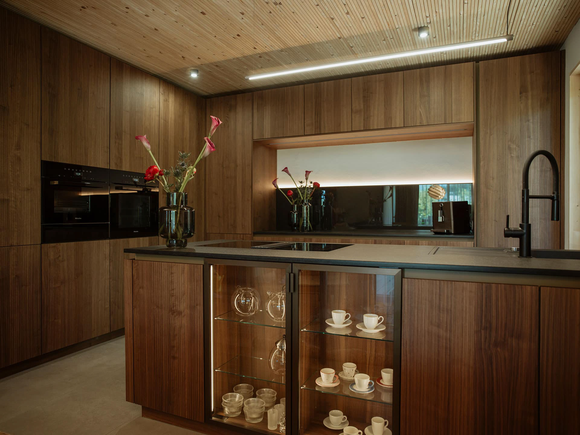 Küche aus Holz mit schwarzen Elementen und Glasvitrine